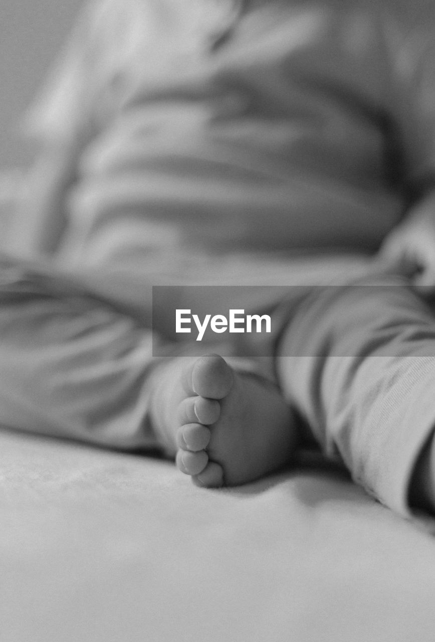 furniture, indoors, bed, black and white, person, white, one person, baby, lying down, relaxation, child, bedroom, close-up, domestic room, monochrome photography, childhood, adult, toddler, arm, human leg, hand, monochrome, sleep, black, lifestyles, selective focus, sleeping, women, men, home interior, resting, sitting, limb, human foot, emotion, barefoot