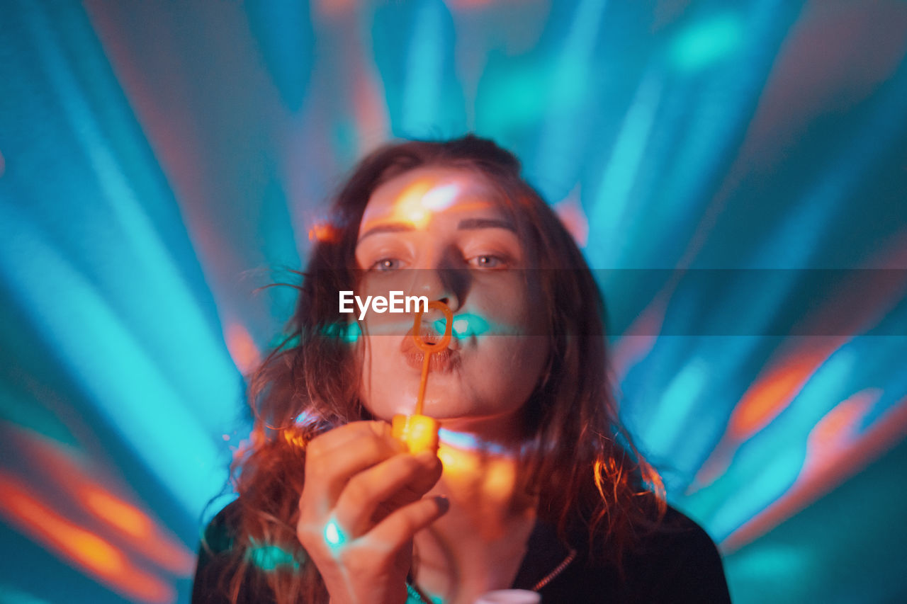 Portrait of woman blowing bubbles against illuminated lights