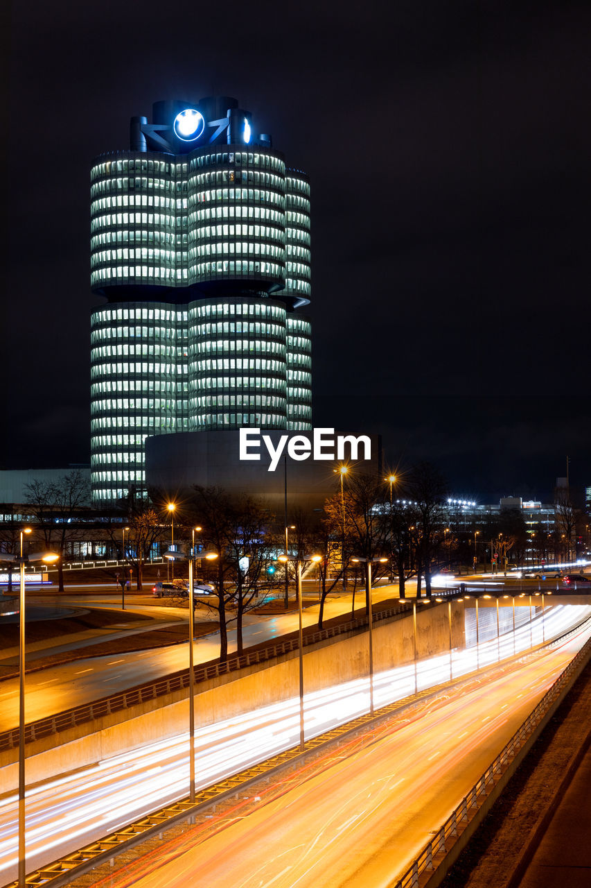 LIGHT TRAILS ON ROAD AGAINST ILLUMINATED BUILDINGS IN CITY AT NIGHT