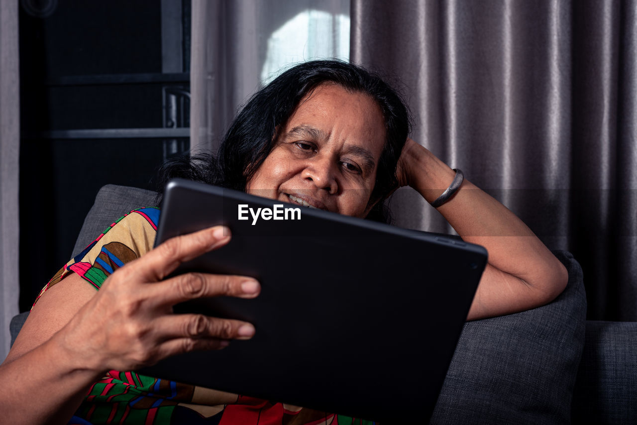 Smiling woman watching movie on digital tablet at home