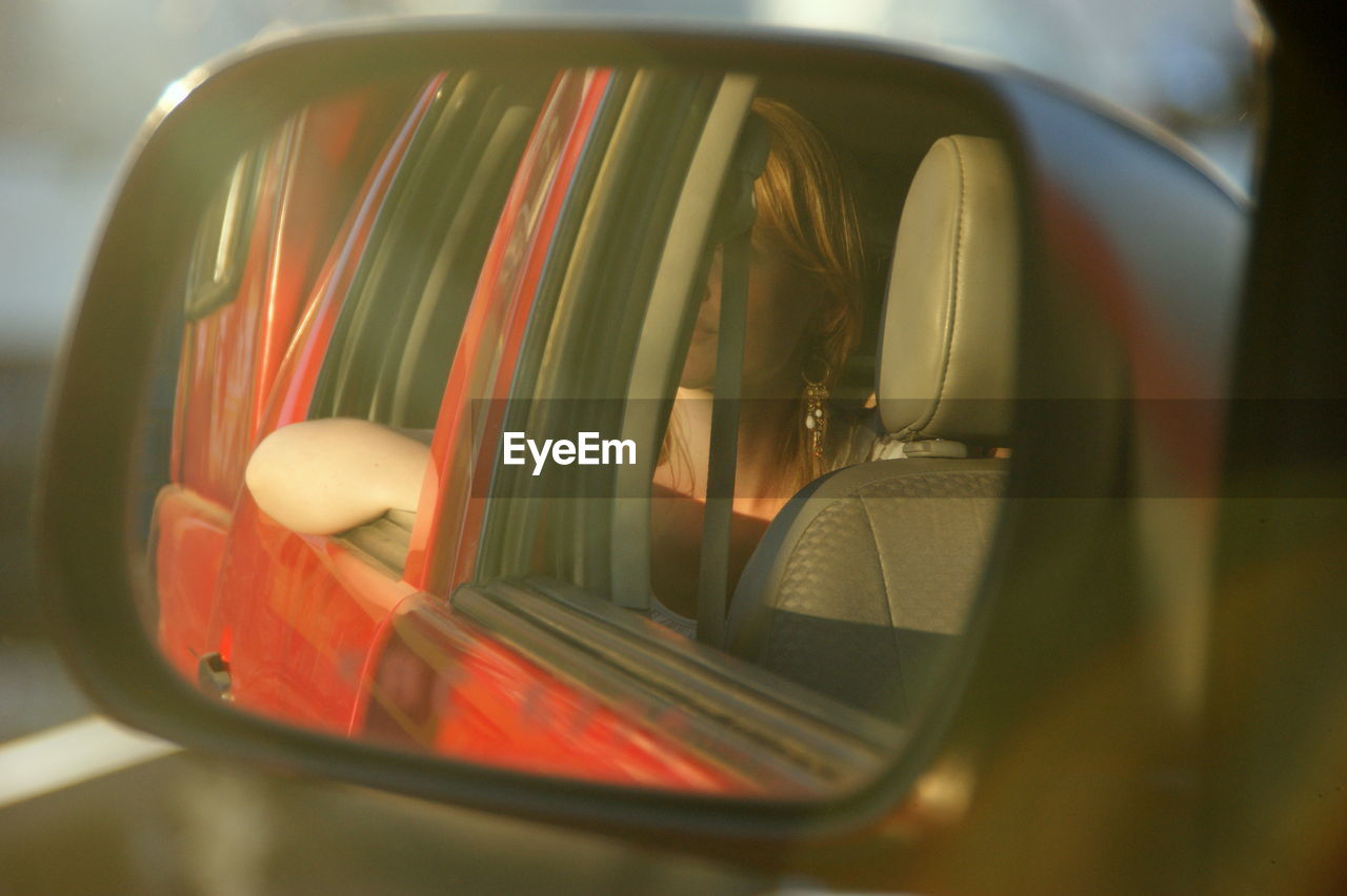 Reflection of woman sitting in car on side-view mirror