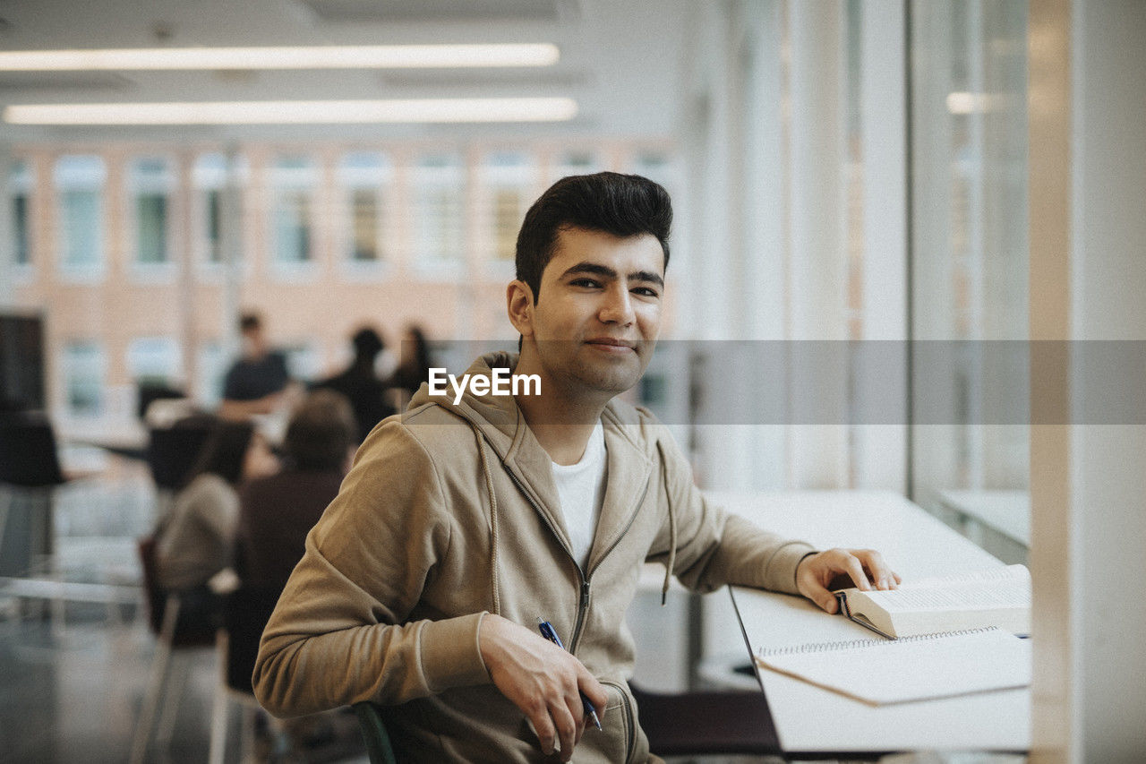 Portrait of smiling male student sitting at table in university