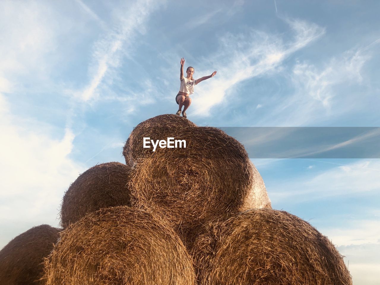 Low angle view of woman crouching on hay bale against sky