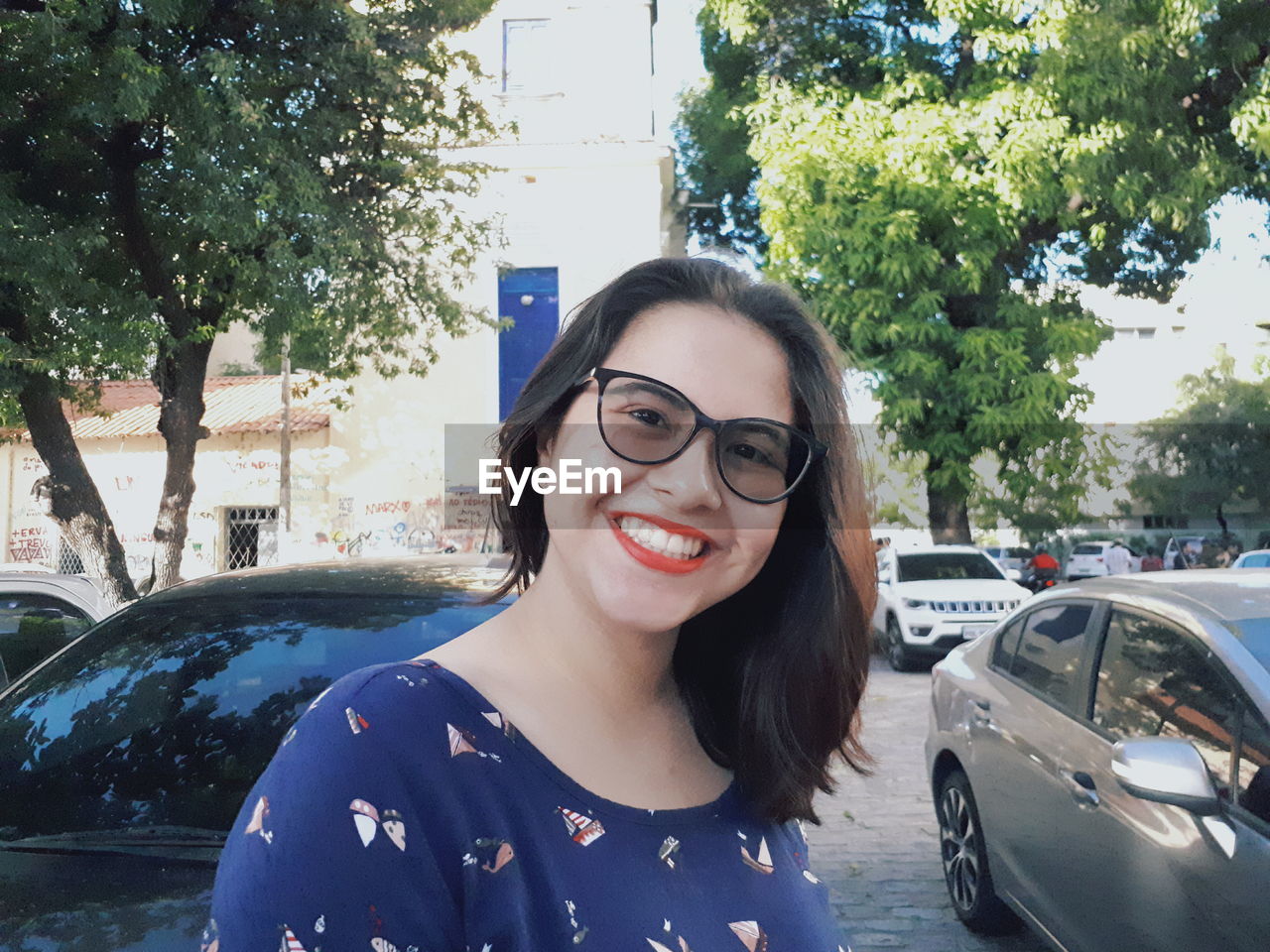 Portrait of smiling young woman standing by cars on street