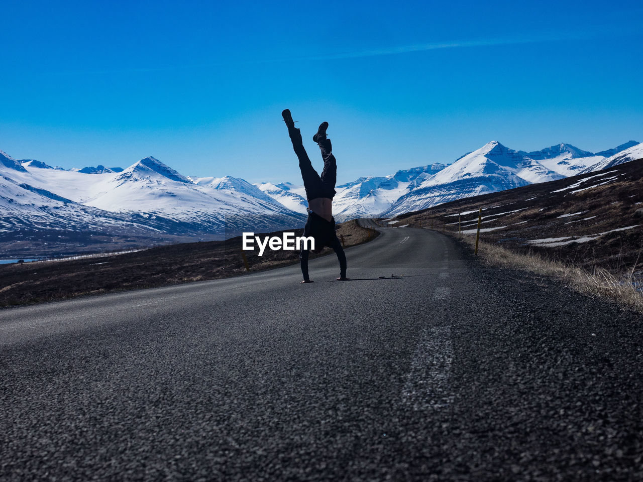 Full length of man doing handstand on road against snowcapped mountains