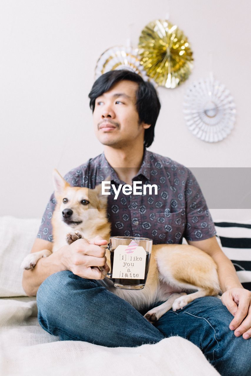 Thoughtful man with dog holding drink at home