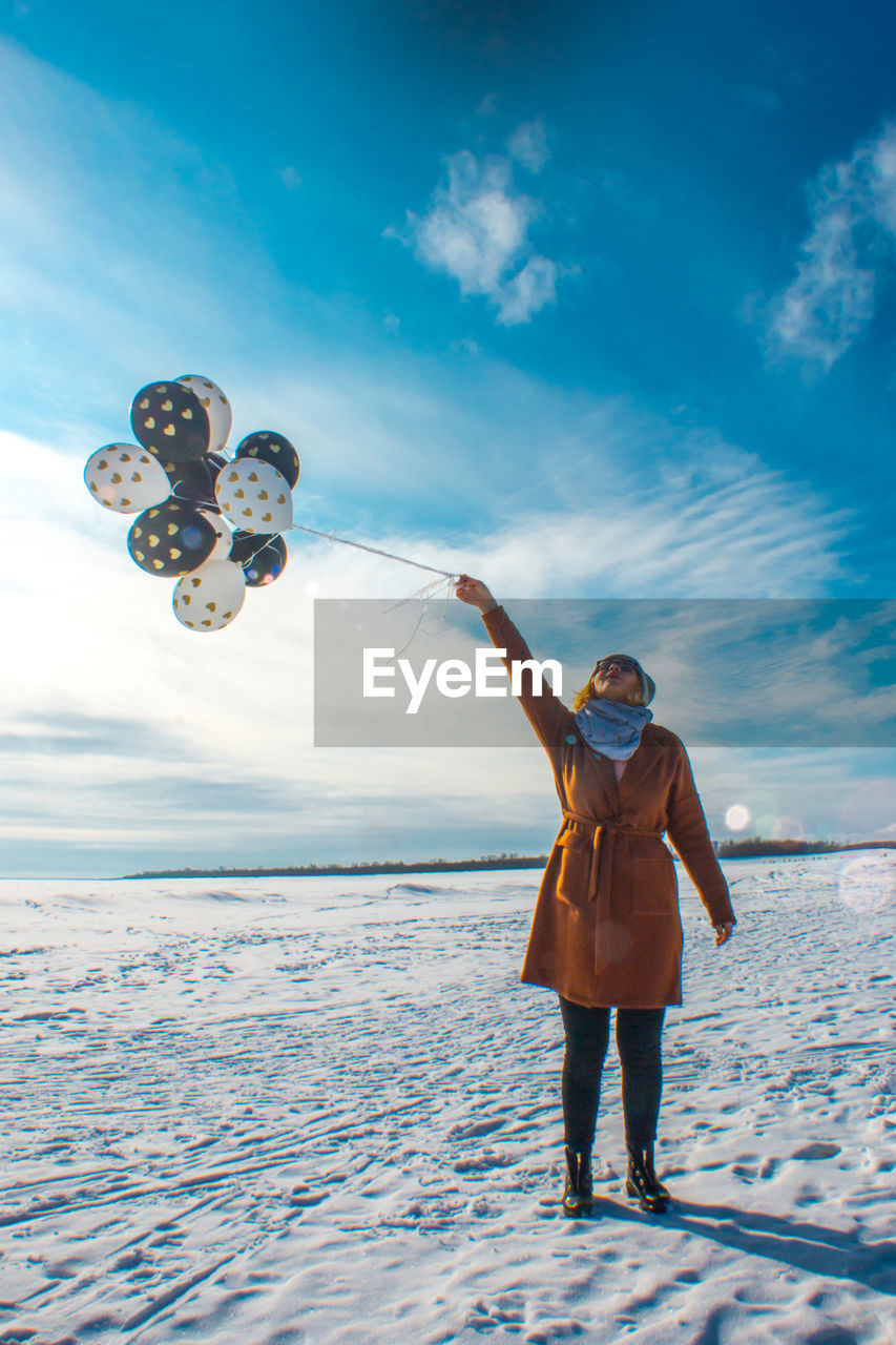 Woman with balloons standing on snow against sky