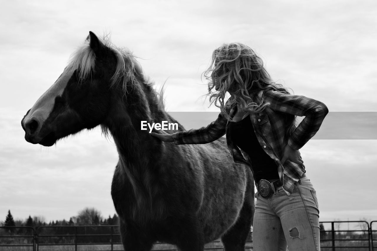 Low angle view of woman petting horse against sky