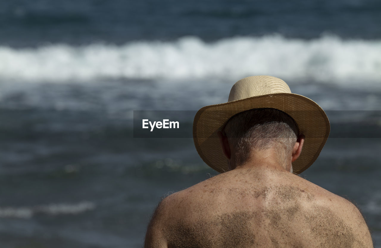 Rear view of shirtless man in hat against se