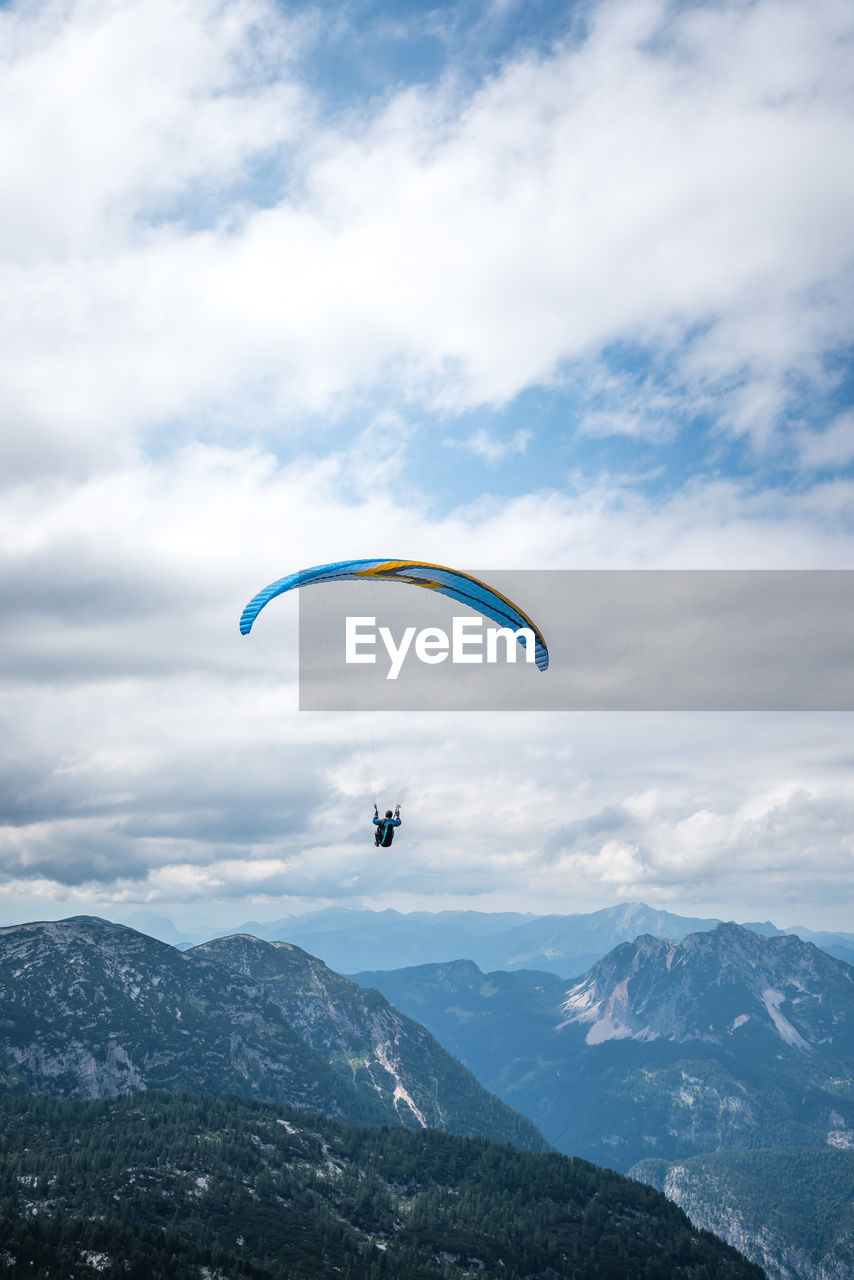 LOW ANGLE VIEW OF MAN PARAGLIDING AGAINST MOUNTAIN