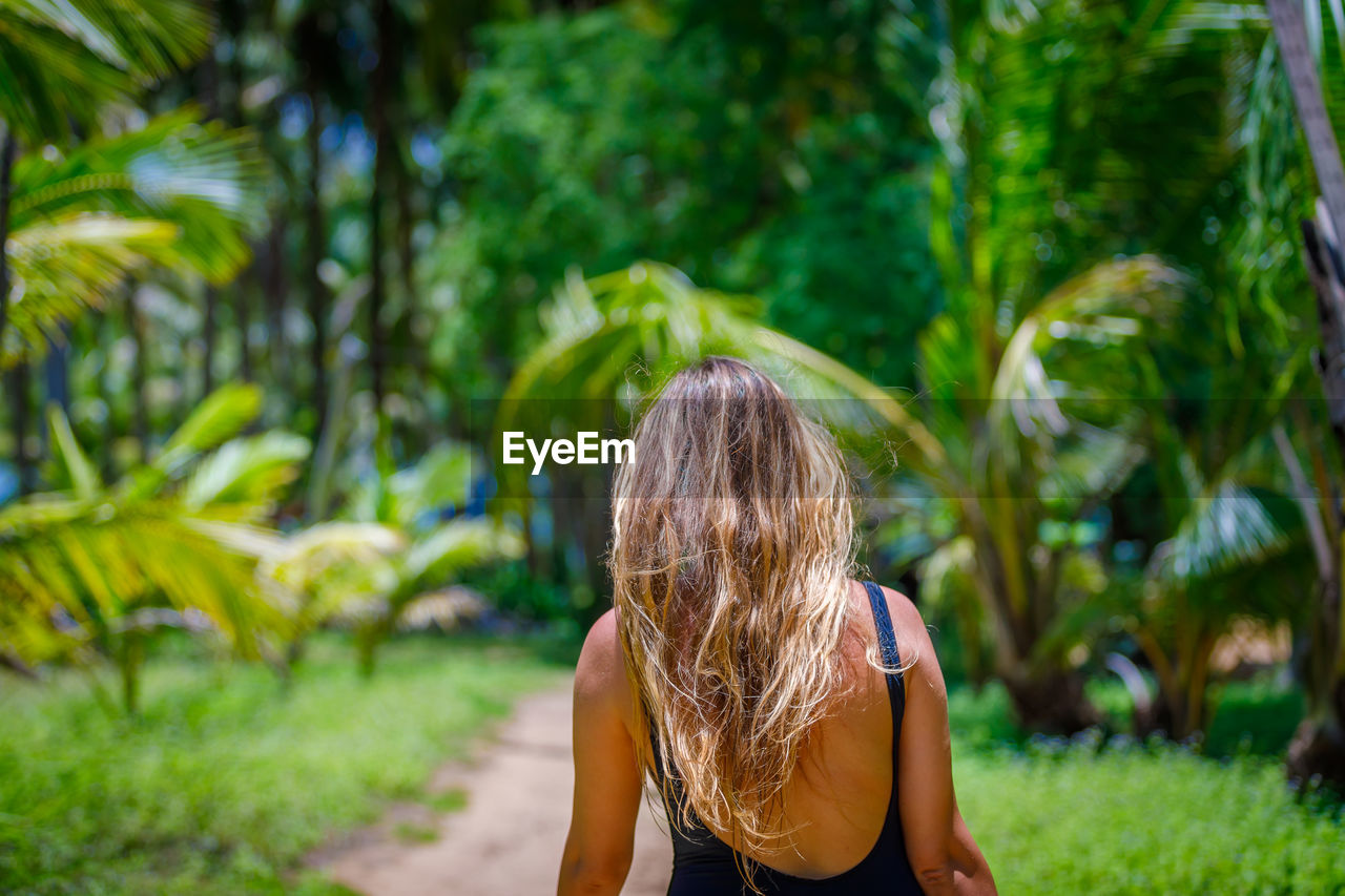 A young girl with blond long hair walks through a palm forest. high quality photo