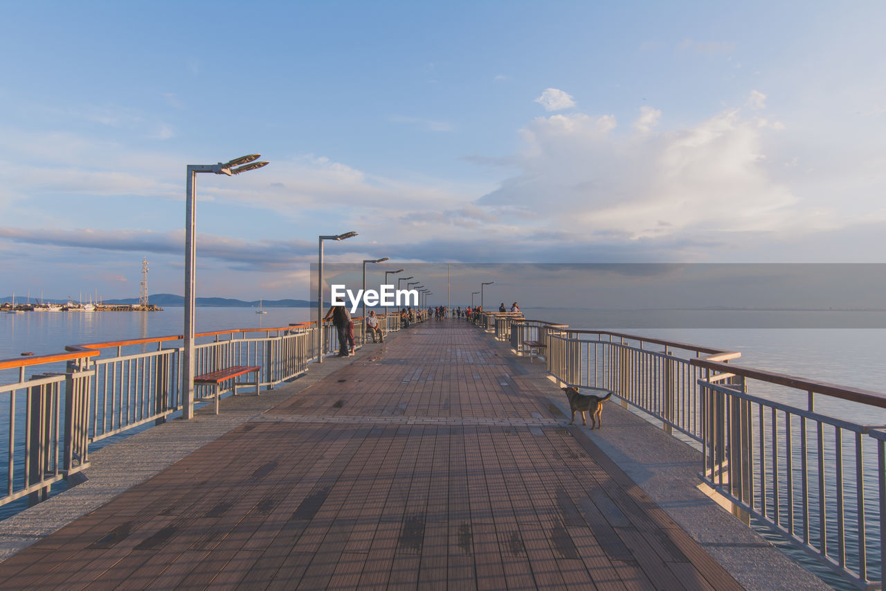 People on bridge over seascape against cloudy sky