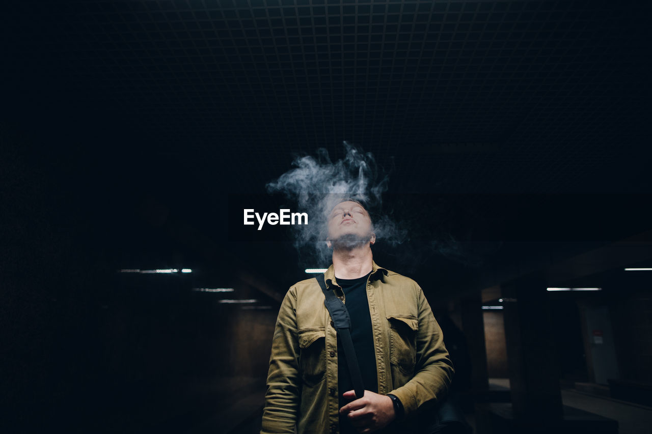 Man smoking while standing in darkroom