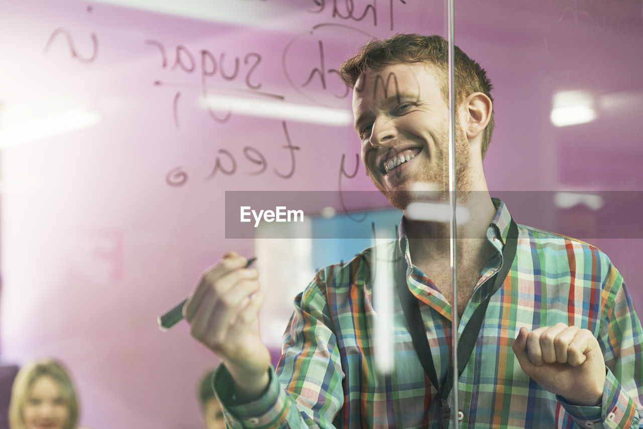 Smiling businessman writing on glass wall during meeting