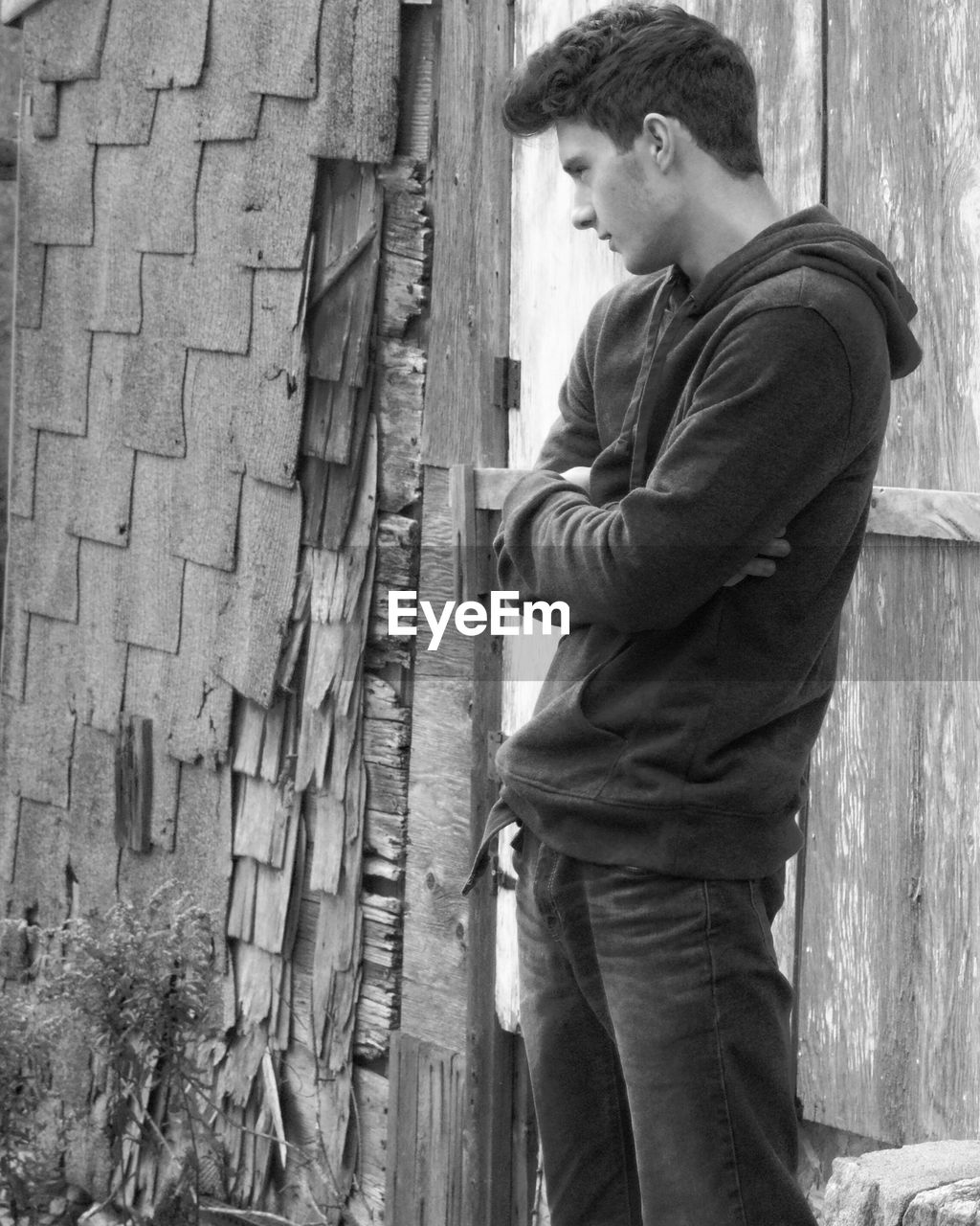 Thoughtful young man with arms crossed standing by old house