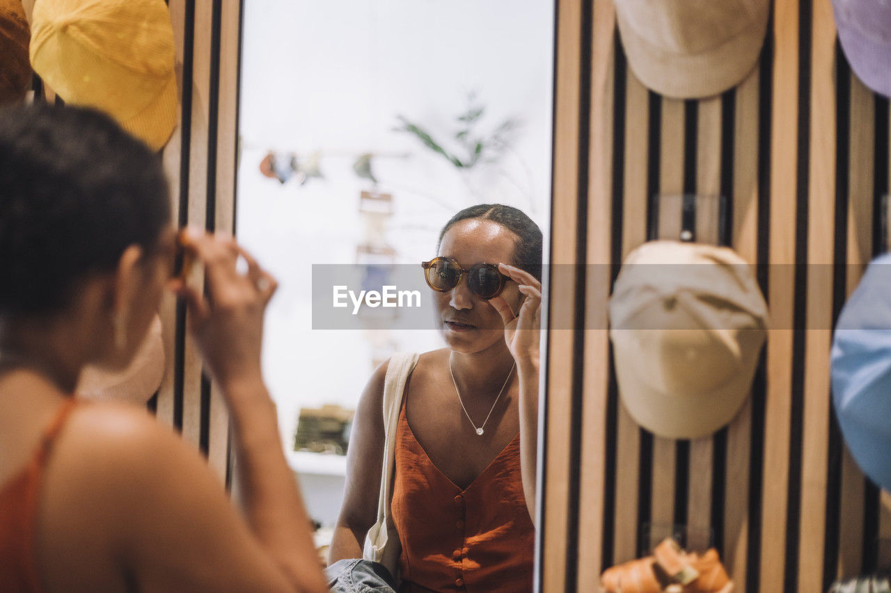 Woman trying sunglasses while looking at reflection in fashion boutique