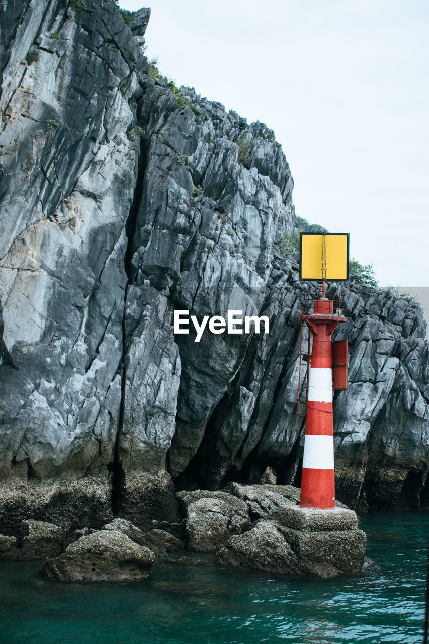 Lighthouse on cliff by sea against sky