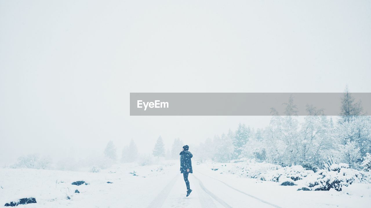 Rear view of woman jumping on snow covered landscape