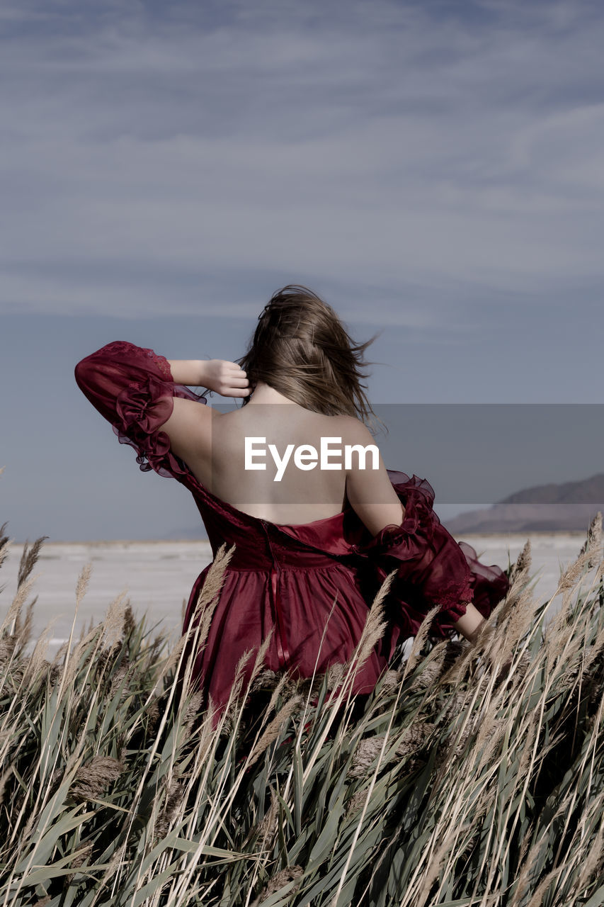 Rear view of teenage girl standing amidst plants on field against sky