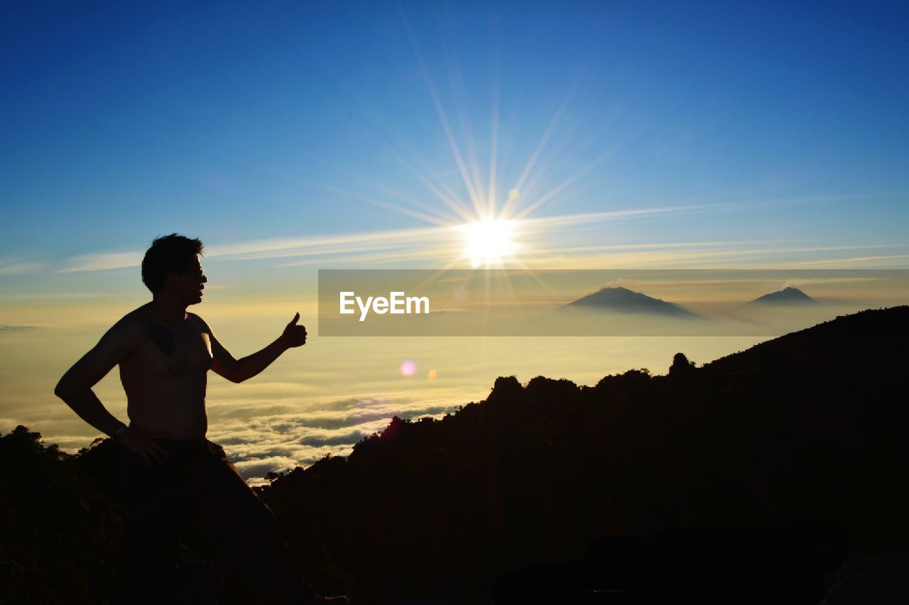 Silhouette man showing thumbs up on mountain peak against sky at sunset