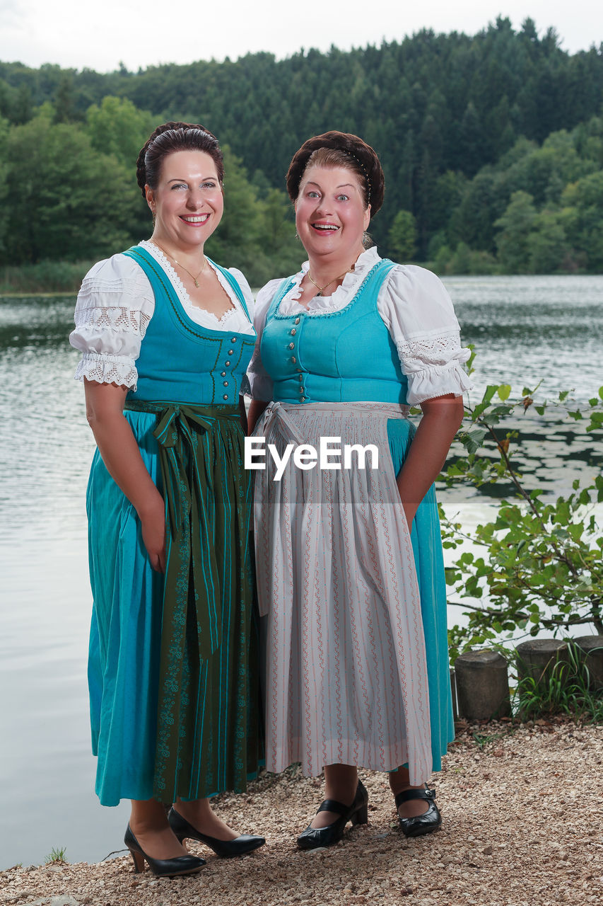 Portrait of smiling female friends standing at lakeshore