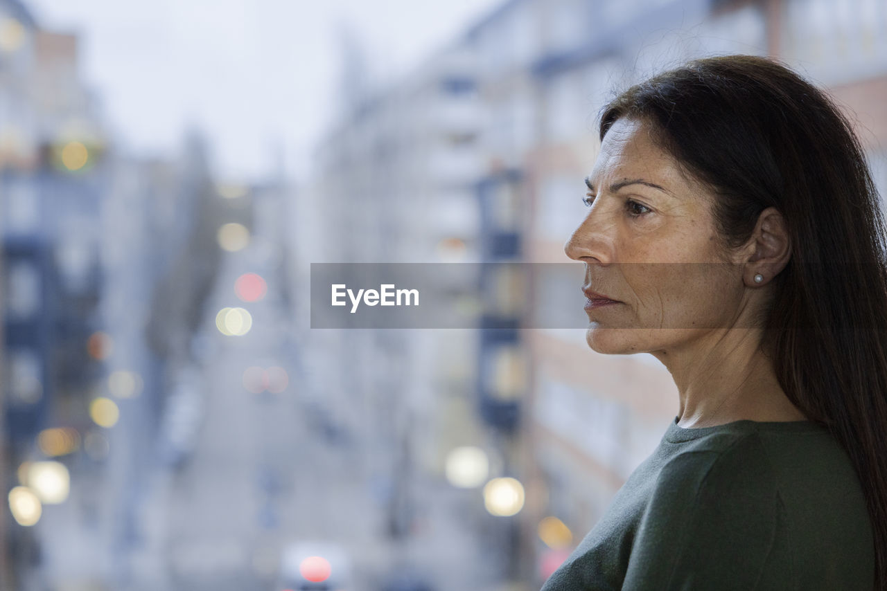 Profile view of mature woman standing next to window