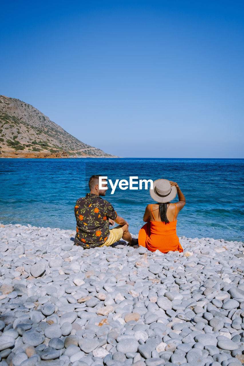 Rear view of couple sitting at seashore against sky