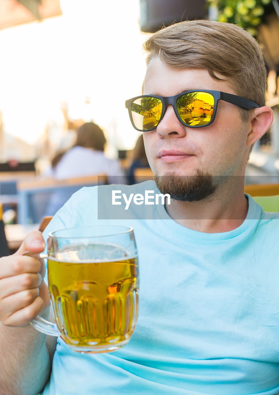 PORTRAIT OF YOUNG MAN DRINKING GLASS ON SUNGLASSES