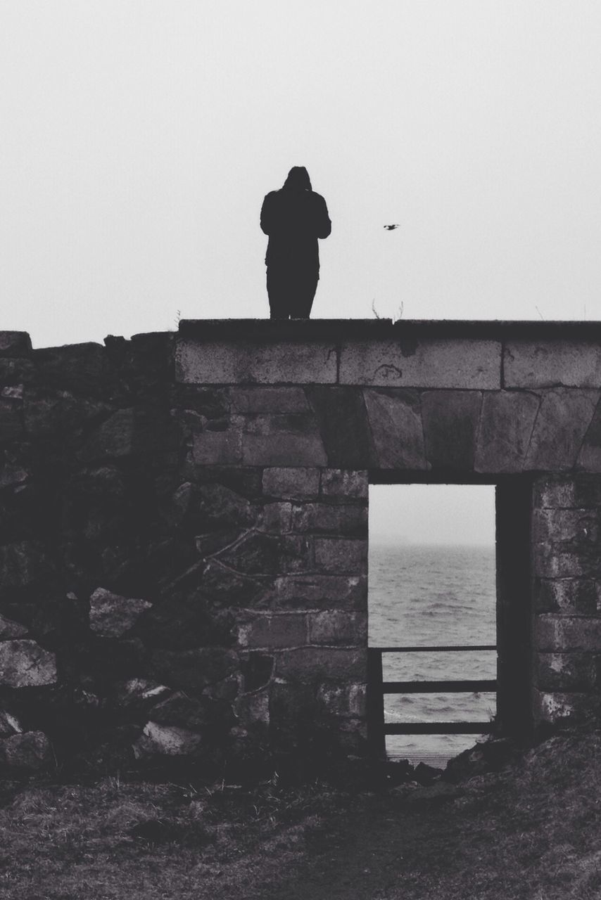 Person standing on stone wall looking at sea view