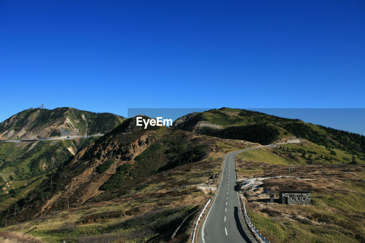 Road leading towards mountain against clear blue sky