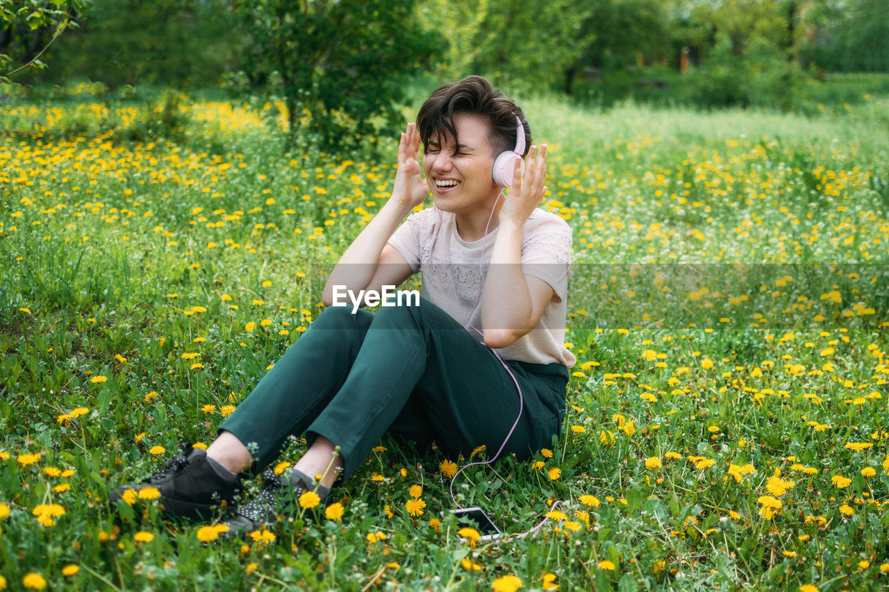 Young beautiful woman sitting on the lawn green grass with dandelions and listen to music 