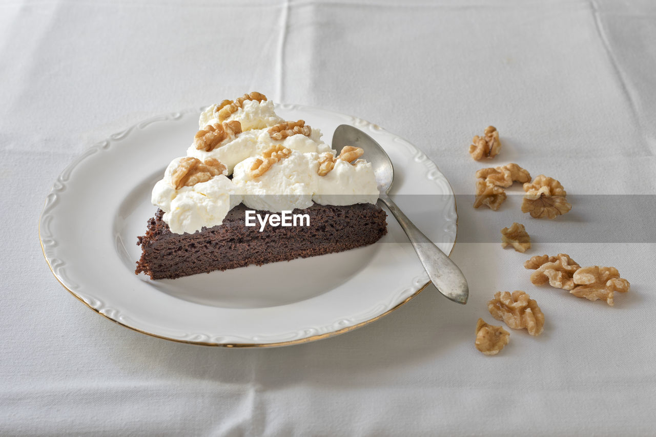 Slice of chocolate cake with whipped cream and walnuts.