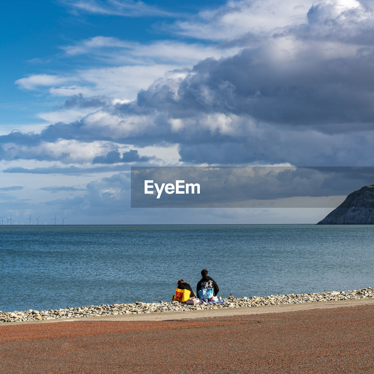 Couple sitting by sea against sky