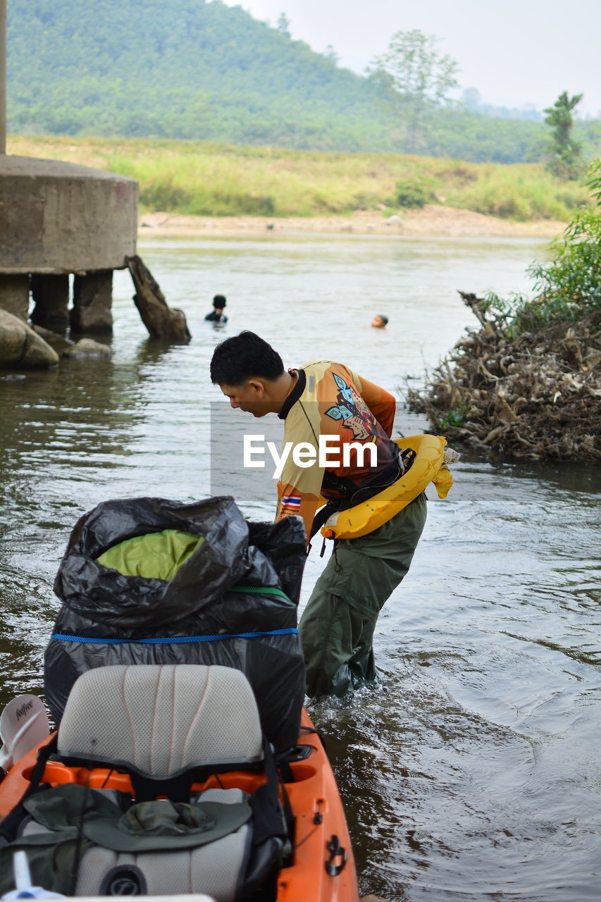 REAR VIEW OF MEN SITTING ON RIVER