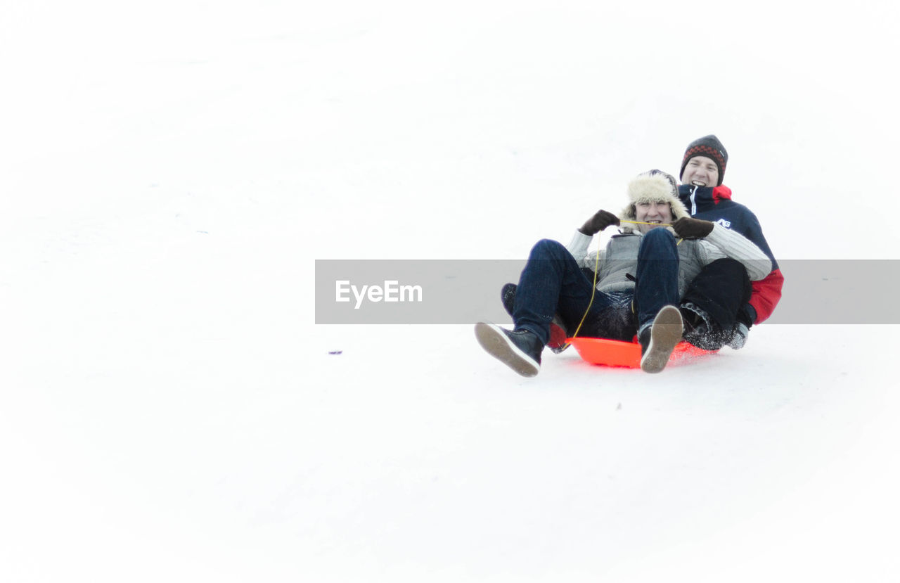 Low angle view of smiling men sledging on snow