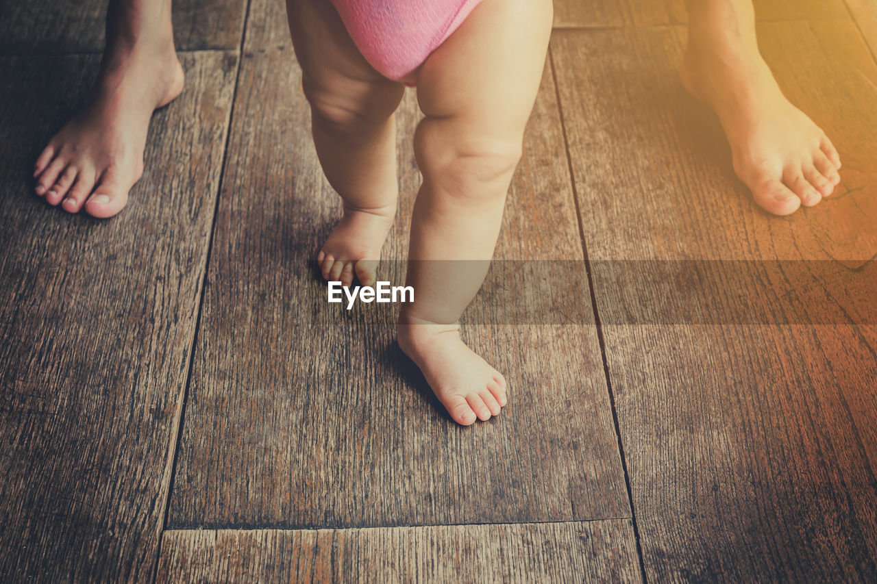 Low section of mother and baby standing on hardwood floor