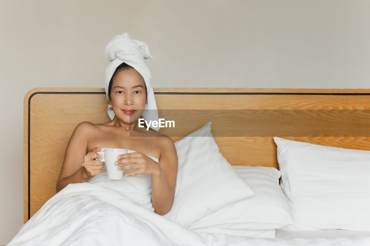 Portrait of young woman sitting on bed at home