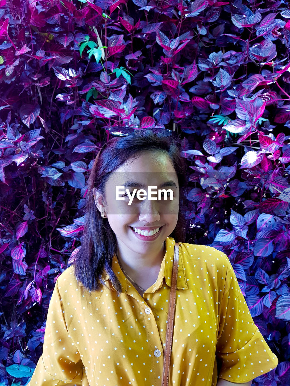 Portrait of smiling young woman standing against purple plants