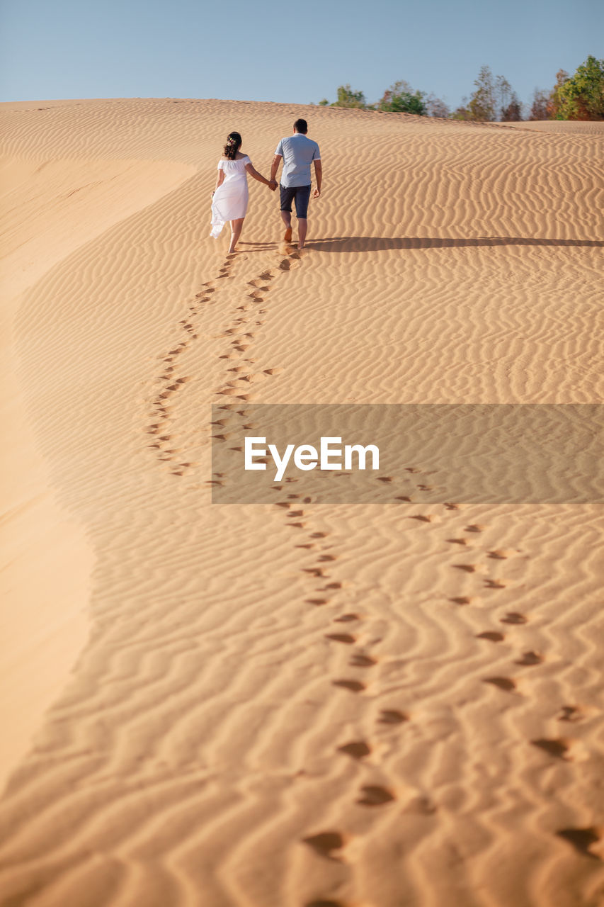 Rear view of couple walking on sand at desert