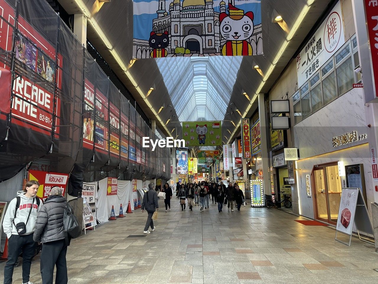 architecture, city, group of people, built structure, crowd, walking, infrastructure, large group of people, building exterior, shopping mall, travel, travel destinations, city life, urban area, street, shopping, text, transportation, store, transport, tourism, retail, women, adult, lifestyles, building, men, public transport, leisure activity, road