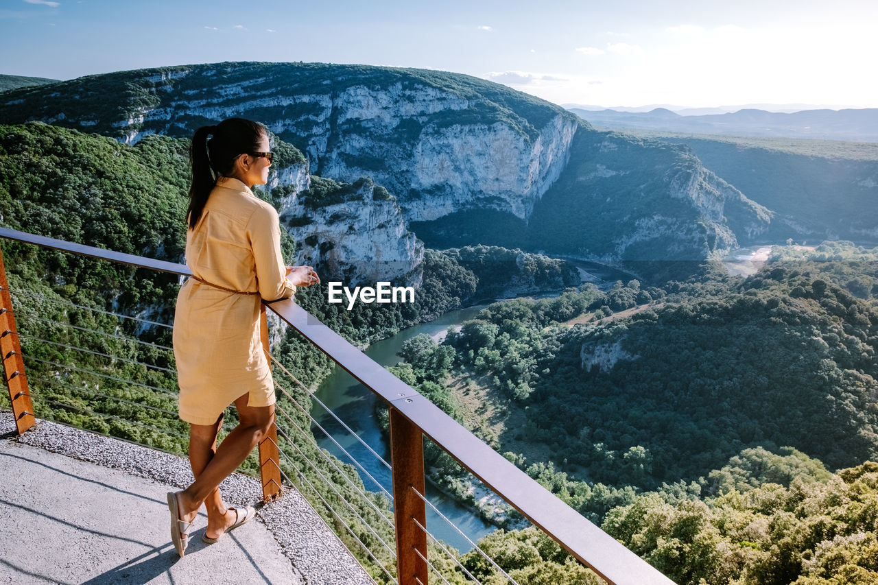 WOMAN STANDING BY RAILING ON MOUNTAIN