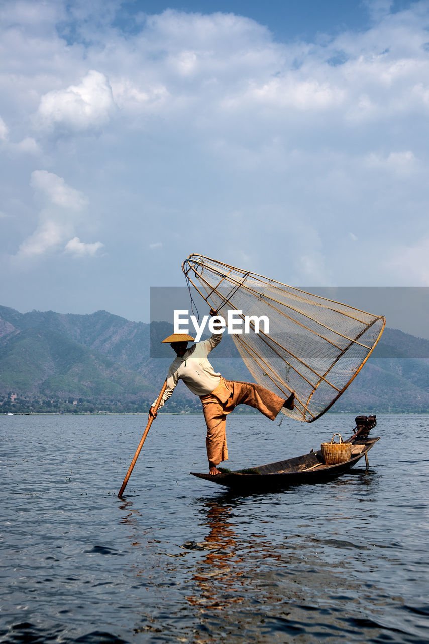 LOW ANGLE VIEW OF PERSON HOLDING FISHING BOAT AGAINST SKY