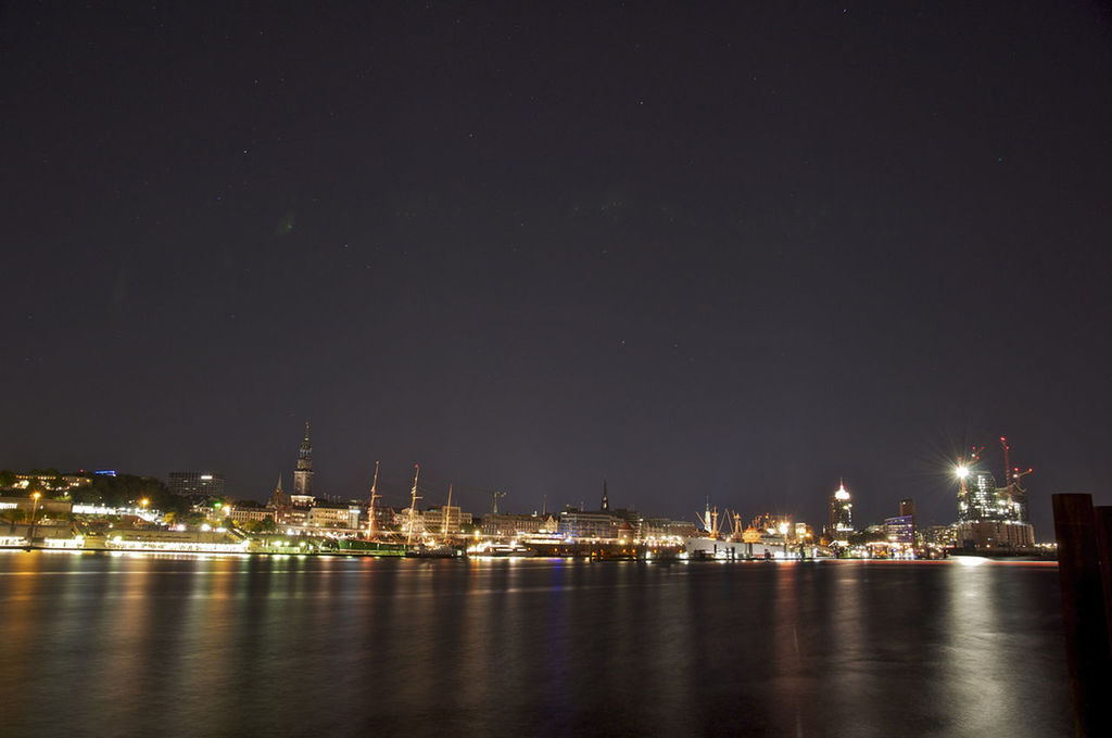 Illuminated city by lake against clear sky at night