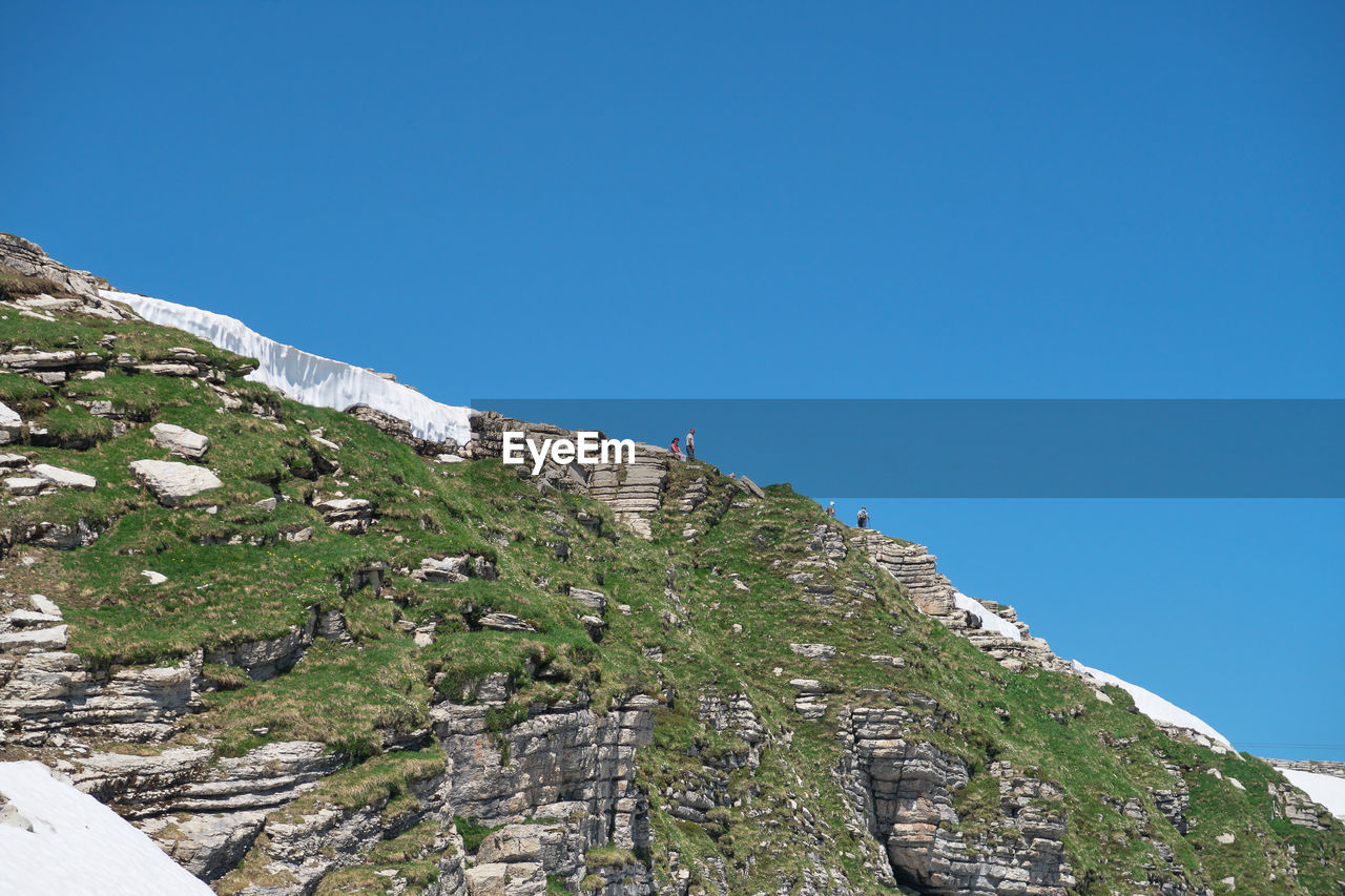 Low angle view of rocky mountain against clear blue sky