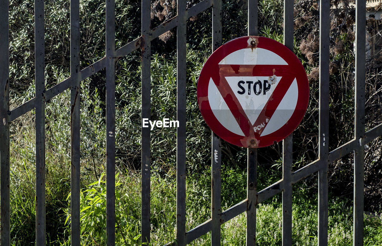 Stop sign on metallic gate against plants