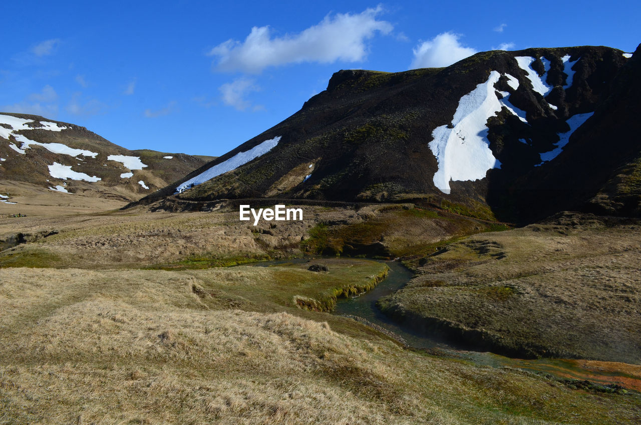 Landscape with a hot spring river and snow on surrounding mountain sides.