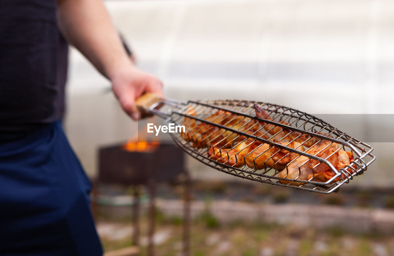 Midsection of man holding meat on barbecue grill
