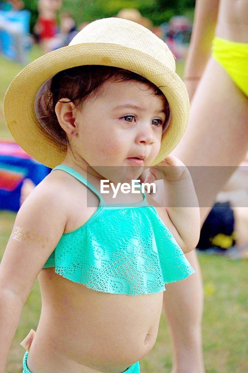 Side view of baby girl wearing swimwear and hat standing on field