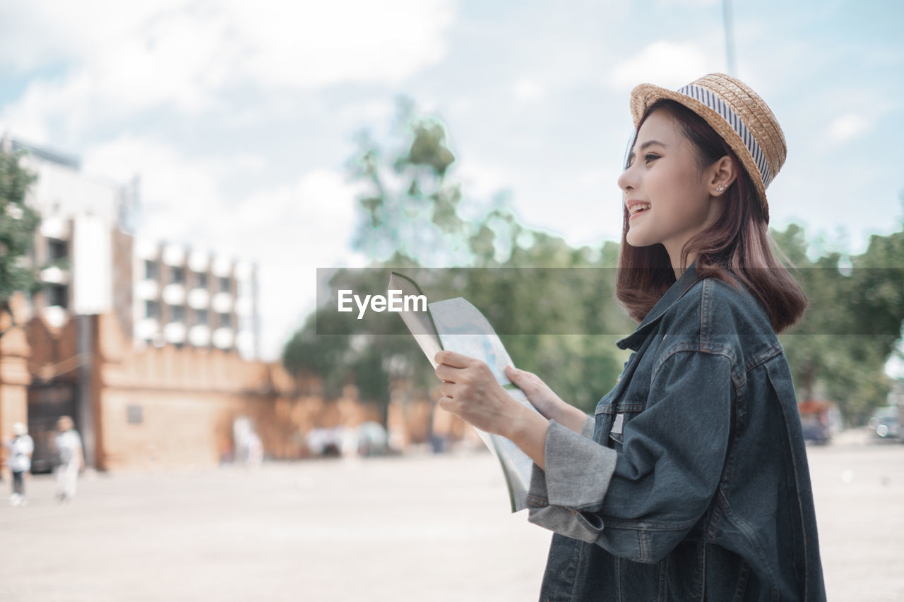 YOUNG WOMAN USING PHONE WHILE STANDING ON CITY