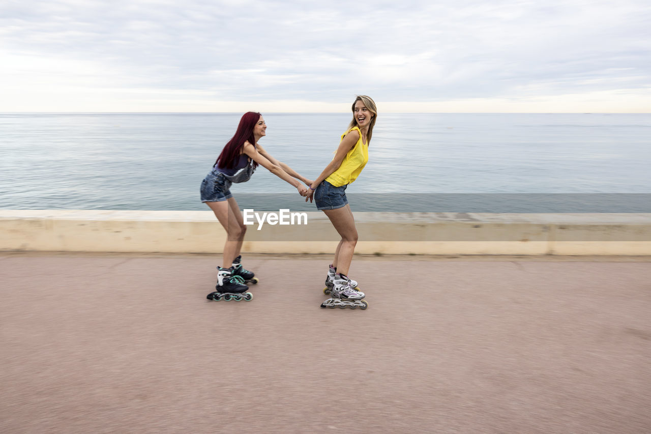 Friends roller skating and having fun at promenade by sea